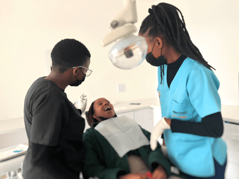 Dental professionals wearing masks assisting a smiling patient during a dental procedure in a clinic.