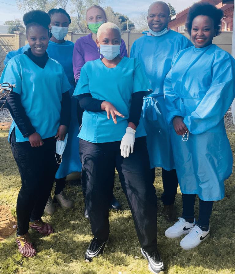 Team of dental professionals in scrubs and masks posing outdoors.